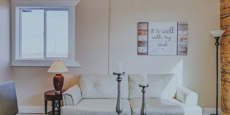 A peaceful living room with a cozy white sofa, soft lighting, and a calming wall sign that reads "It is well with my soul," creating a serene atmosphere.