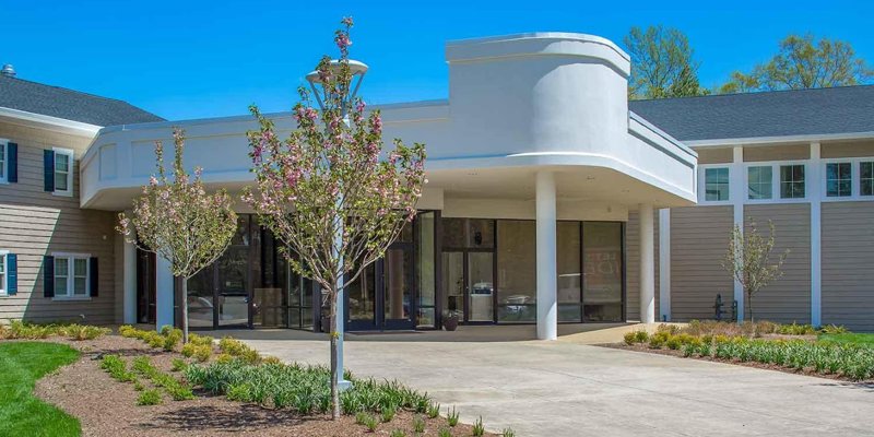 Inviting entrance to a rehabilitation center with a modern design, blooming trees, and well-manicured landscaping under a bright, clear sky.