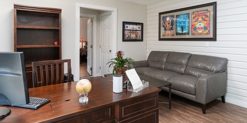 A welcoming office space featuring a wooden desk, comfortable leather couch, potted plant, and framed artwork, offering a cozy atmosphere.