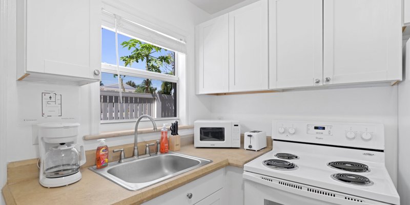 A bright and compact kitchen with white cabinets features a clean countertop, essential appliances, and a window that lets in natural light.