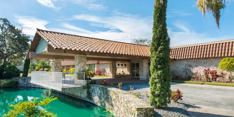 Charming entrance with a stone bridge over a serene pond, lush greenery, and vibrant landscaping, creating a welcoming atmosphere.