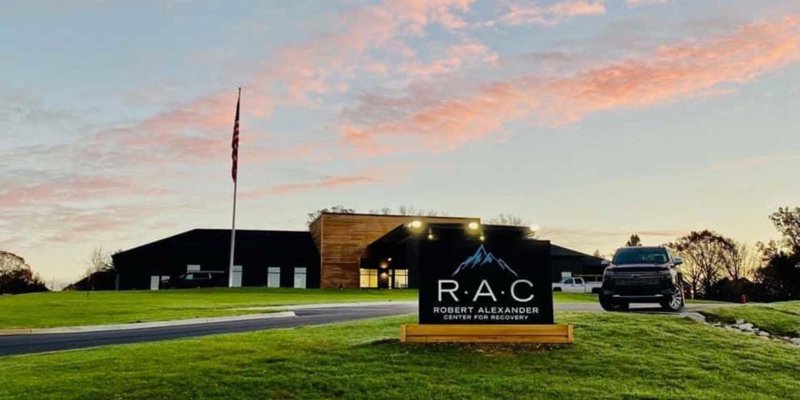 Modern recovery center with a welcoming entrance, well-lit signage, and expansive green lawns, set against a beautiful sunset sky.