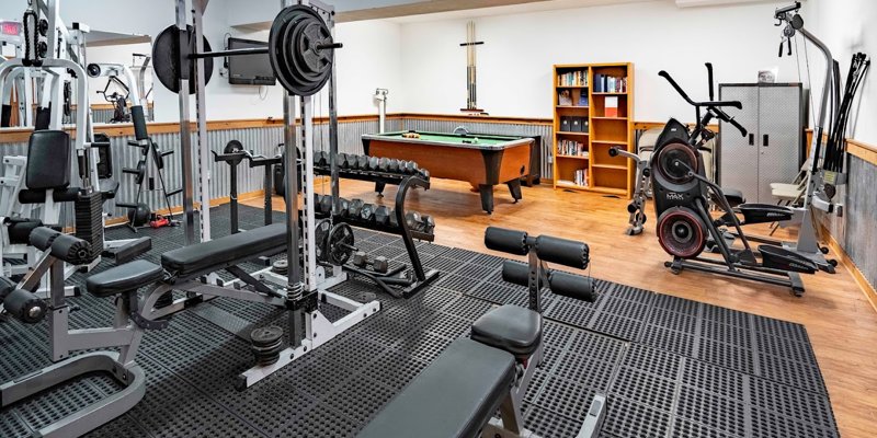 A well-equipped home gym with various fitness machines, weights, and a pool table, offering a balanced mix of recreation and exercise.