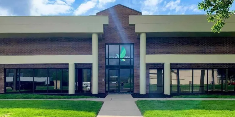  Bright entrance of a rehab facility with large windows, brick facade, and lush green lawn, creating a welcoming and professional atmosphere.