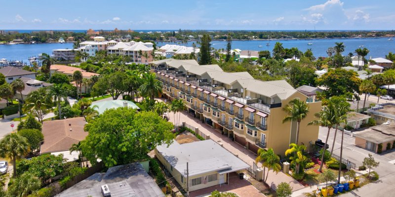 Aerial view of a serene coastal neighborhood with lush greenery, vibrant homes, and waterfront access, offering a peaceful, scenic setting.