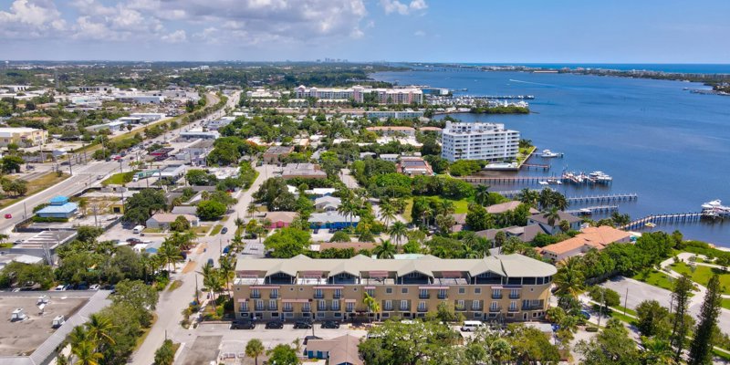 Aerial view of a vibrant coastal town with scenic waterfront properties, lush greenery, and a beautiful marina, offering serene ocean views.