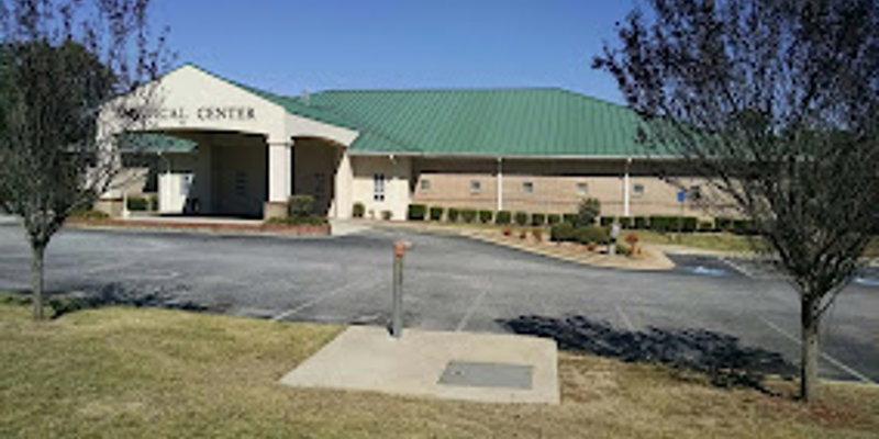  A medical center with a welcoming entrance, light-colored brick walls, a green roof, and a well-maintained landscape, creating a serene setting.