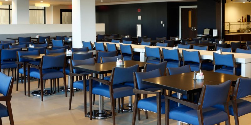 A spacious dining area with modern tables and comfortable blue chairs offers a clean and inviting environment for meals and socializing.