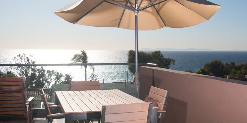 Sunny patio with wooden dining set and umbrella, offering stunning ocean views and a serene ambiance, perfect for outdoor meals.