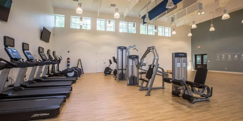 Spacious fitness center with modern exercise equipment, bright natural light from high windows, and wooden floors, perfect for a revitalizing workout.