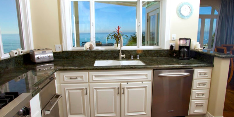 A bright kitchen with modern appliances, marble countertops, and white cabinetry offers stunning ocean views through large windows.