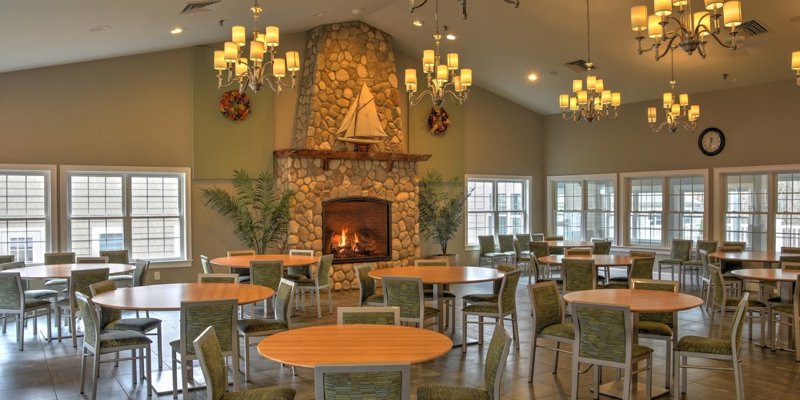 A warm, inviting dining area featuring a stone fireplace, elegant chandeliers, and large windows, offering a cozy and welcoming atmosphere.