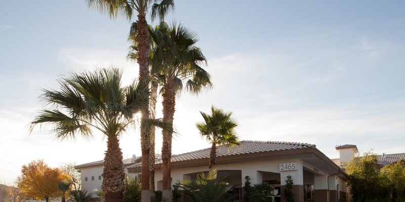 A peaceful exterior view of a rehab center at sunset, framed by tall palm trees, well-kept landscaping, and a warm, inviting atmosphere.