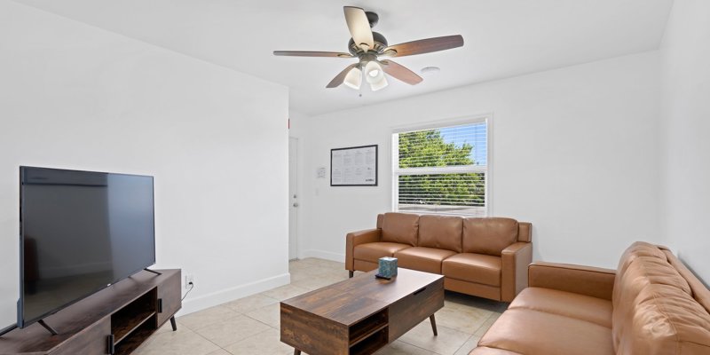 A bright, minimalist living room features modern leather sofas, a large TV, and a wooden coffee table, creating a clean and cozy atmosphere.