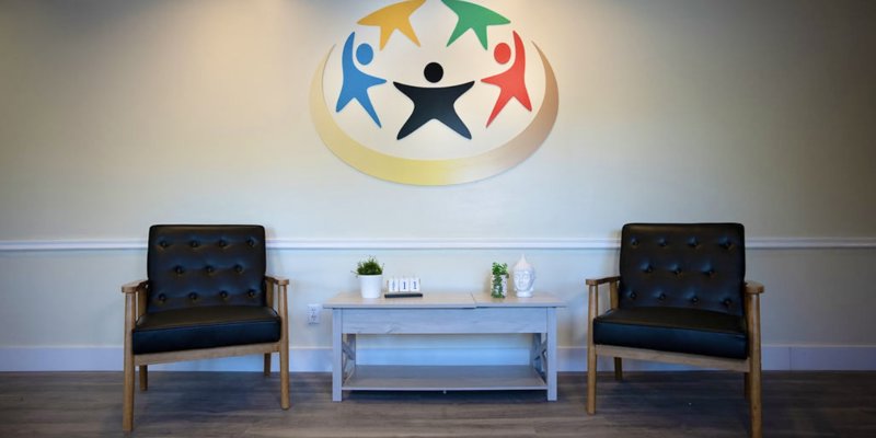  A welcoming seating area with two comfortable chairs and a minimalist table, set against a wall adorned with a colorful, uplifting logo.