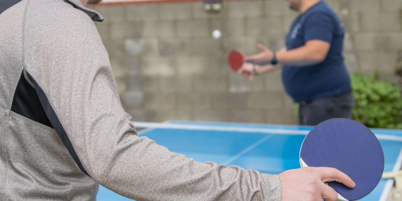 Two people enjoy a friendly game of ping pong outdoors, focusing on the action with paddles in hand and a ball mid-air.