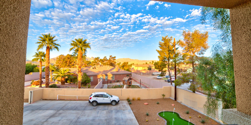 A stunning desert view featuring palm trees, a spacious driveway, and a mini golf setup, with mountains in the distance under a bright, blue sky.