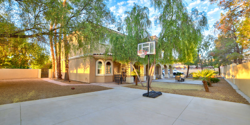 Spacious backyard with a basketball hoop, large trees providing shade, and a cozy seating area, perfect for outdoor activities and relaxation.