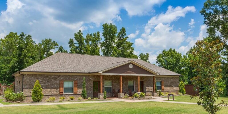  A charming brick home with a well-maintained lawn, surrounded by lush trees and a bright blue sky, creating a peaceful, welcoming vibe.