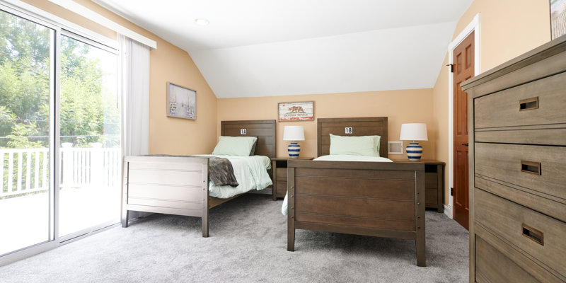 A bright bedroom with two wooden twin beds, soft green bedding, and a sliding glass door leading to a scenic outdoor view. Peaceful and inviting!