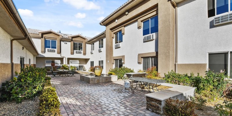 A charming courtyard featuring a fountain, neatly paved walkways, garden seating, and lush greenery, creating a peaceful outdoor retreat.