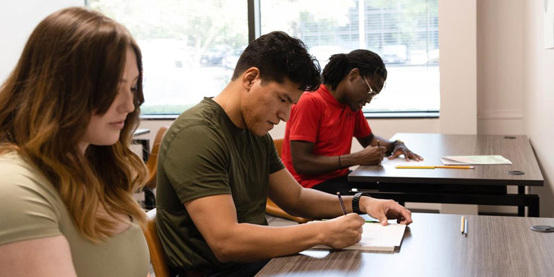 A diverse group of focused individuals participates in a classroom activity, fostering learning and growth in a bright, supportive environment.