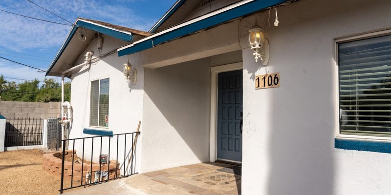 A cozy home with a welcoming blue door and matching trim, brightened by sunlight. The entrance is framed by neat landscaping.