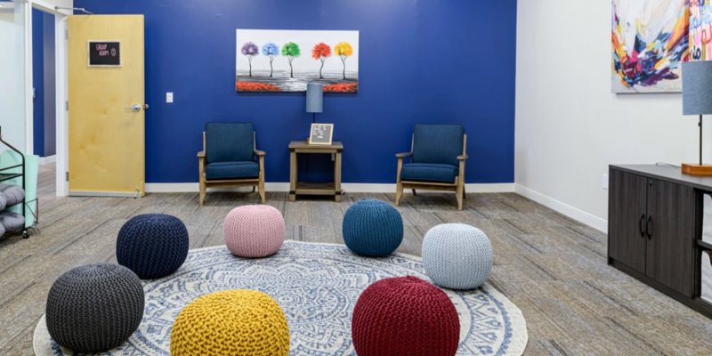 A bright, inviting group therapy room features colorful poufs, cozy chairs, and vibrant artwork, creating a warm and welcoming environment.