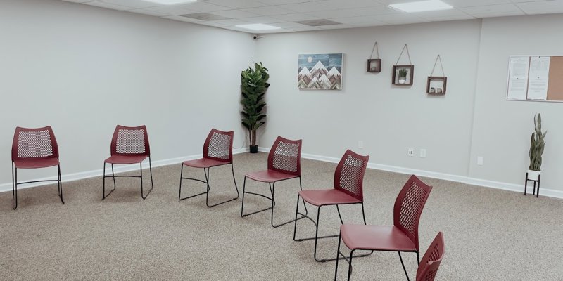 A bright, open room arranged for group meetings, featuring red chairs in a circle, calming decor, and soft lighting, fostering a welcoming environment.