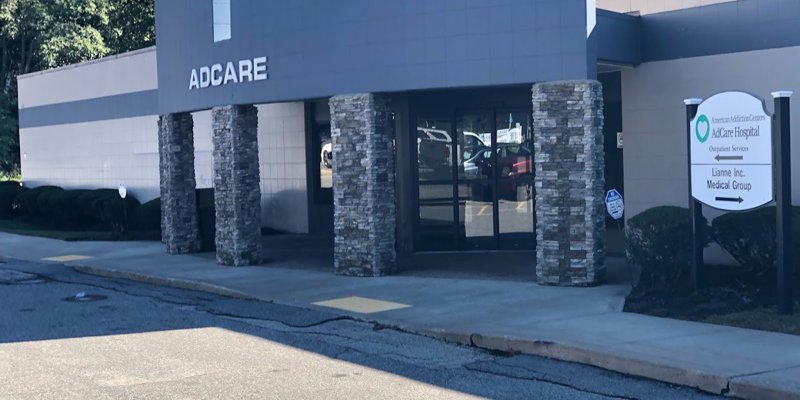 The exterior of a medical facility named "AdCare" with stone pillars at the entrance. A sign also indicates outpatient services nearby.