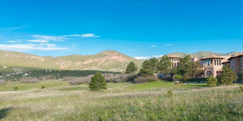 A scenic view of a building nestled in a vast, green landscape with rolling hills and clear blue skies, offering a tranquil and serene setting.