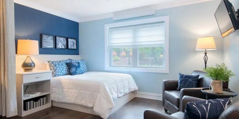  A bright, cozy bedroom featuring a comfortable bed, stylish decor in blue tones, and a seating area, creating a peaceful and inviting space for rest.