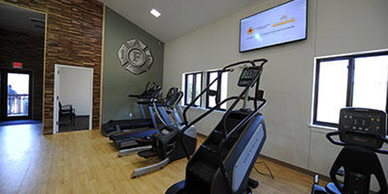 A modern gym with cardio equipment, including treadmills and stair climbers, set in a bright, spacious room with natural light and wooden floors.