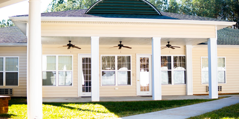 A welcoming porch with white columns, ceiling fans, and large windows, offering a shaded, relaxing outdoor space in a tranquil setting.