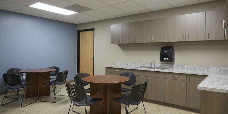  Comfortable break room with modern cabinetry, cozy round tables, and ample seating, offering a relaxed space for conversation and refreshments.