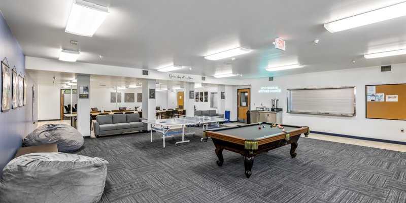 A spacious recreation room featuring a pool table, ping-pong table, cozy couches, and bean bags. Bright lighting creates an inviting atmosphere.