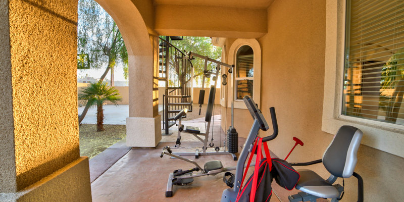 Outdoor workout area with fitness equipment under a covered patio, surrounded by greenery and natural light for an energizing exercise space.