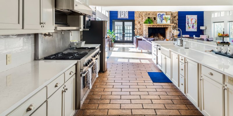  A spacious kitchen with modern stainless steel appliances, bright countertops, and a view into a cozy living area with a stone fireplace.