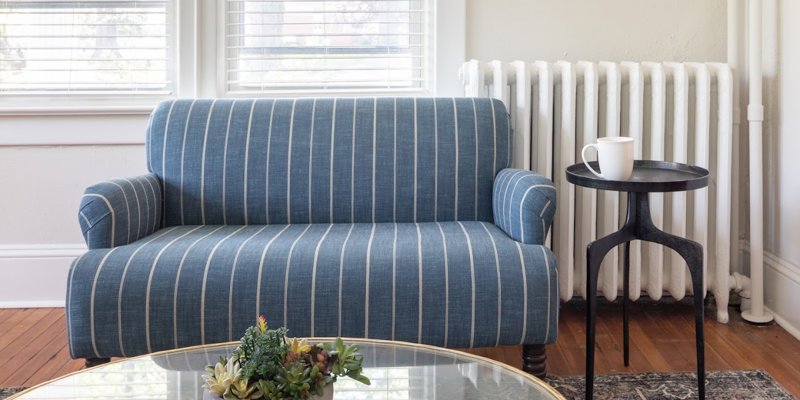 A cozy seating area with a striped blue loveseat, small side table, and glass-top table with succulents. Bright and inviting space.