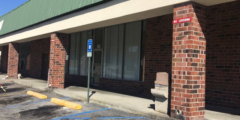 A storefront with brick pillars, a green roof, and accessible parking. The shaded walkway provides a welcoming entrance to the building.