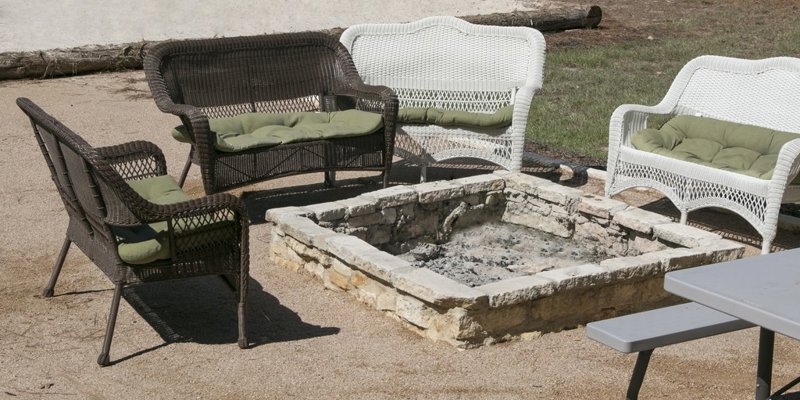 Cozy outdoor seating area featuring wicker furniture with soft cushions, arranged around a stone fire pit, perfect for social gatherings.