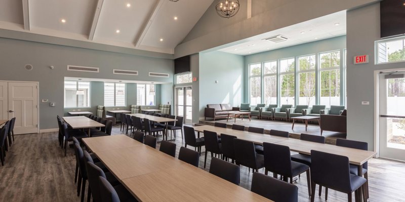 A spacious, bright dining hall with large windows, modern light fixtures, and neatly arranged tables and chairs, creating a welcoming environment.