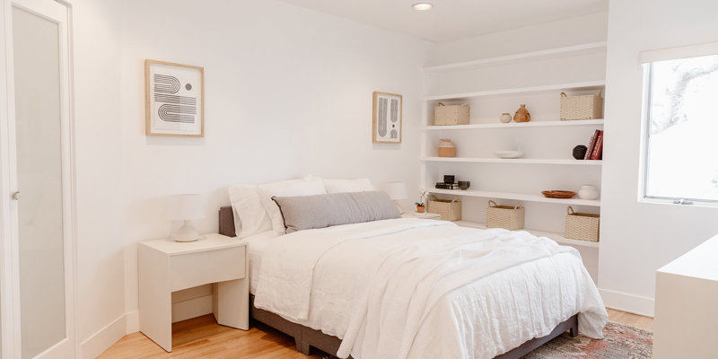  A bright, minimalist bedroom with a cozy bed, soft white bedding, built-in shelves, and a modern aesthetic for a serene atmosphere.