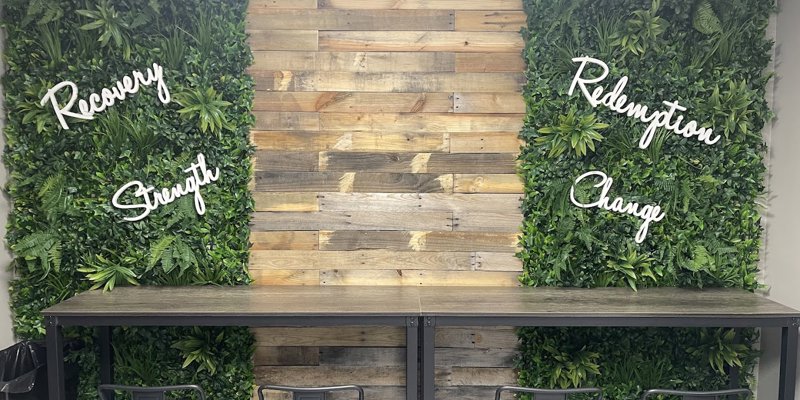  A welcoming wall display with greenery and motivational words like "Recovery," "Strength," "Redemption," and "Change," paired with high-top seating.