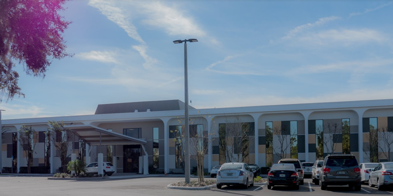 A modern, welcoming facility with ample parking, highlighted by sleek architectural lines and a bright, clear sky in the background.