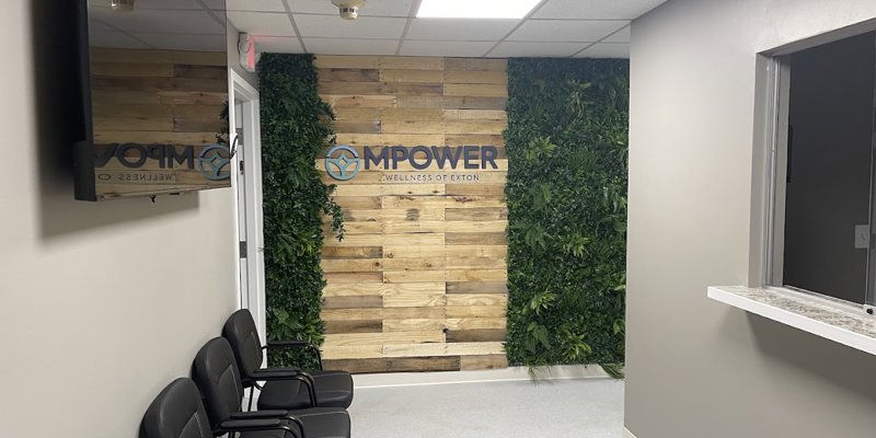  A modern, welcoming lobby with a wood accent wall, greenery, and comfortable seating. The "Mpower Wellness" logo adds a professional touch.