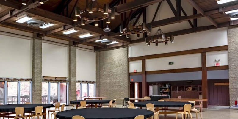 A spacious, rustic hall with high, wooden-beamed ceilings and large windows, creating a warm and inviting atmosphere for gatherings.