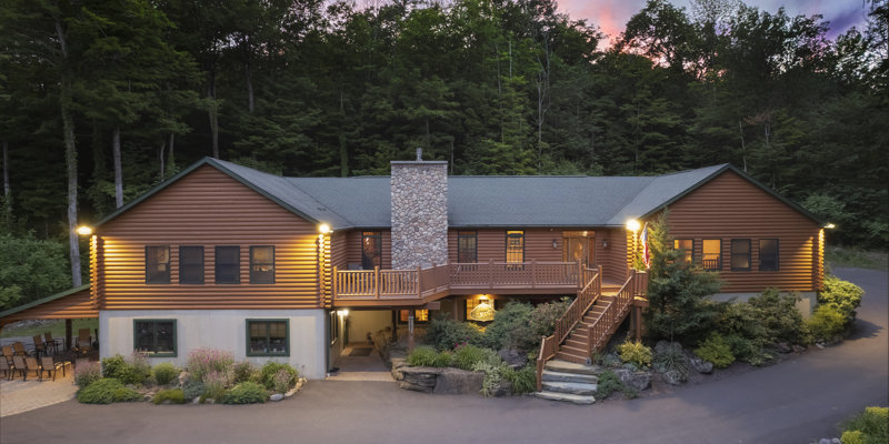 A beautifully lit log cabin nestled in lush greenery at dusk, offering a warm and inviting atmosphere with rustic charm and serene surroundings.