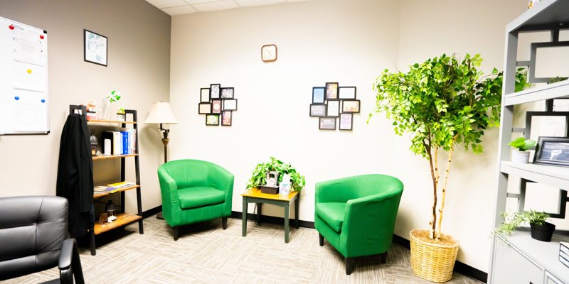 Bright, welcoming office with green chairs, potted plants, inspirational wall decor, and a bookshelf, creating a calming and inviting atmosphere.