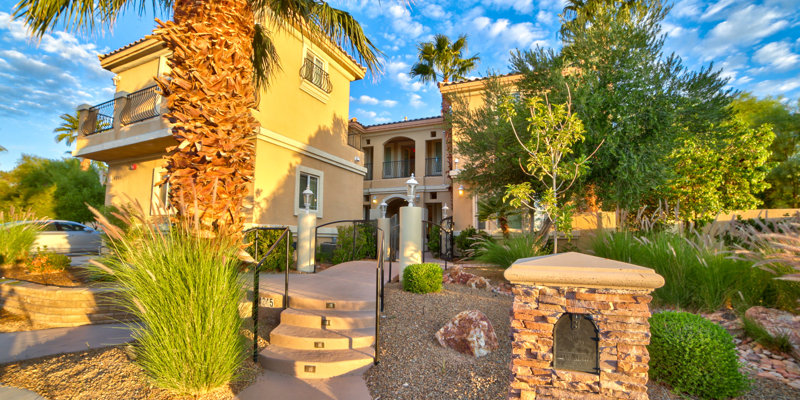 A beautiful Mediterranean-style home surrounded by lush landscaping, palm trees, and warm sunlight, with a welcoming entryway and stone mailbox.